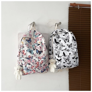 Detailed view of two butterfly print backpacks hanging on a wall with plush bear charms