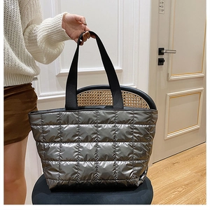 Detail of silver quilted puffer tote bag with black straps on a chair in a room