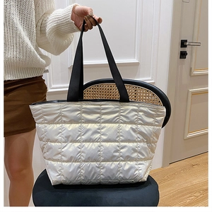Close-up of white quilted down tote bag on black chair showing soft texture and straps