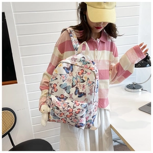 Detailed view of a white backpack featuring colorful butterfly patterns and a bear charm