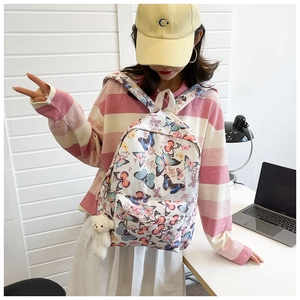 Detail of colorful butterfly print backpack featuring front zip pocket and plush bear charm