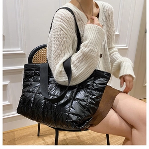 Detail of black quilted down tote bag with glossy finish and wide woven shoulder strap