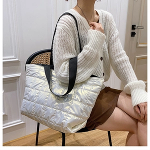 Iridescent silver quilted down tote bag with black nylon straps shown on a model