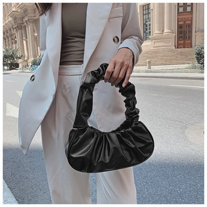 Detail of black pleated croissant bag texture shown on a white suit jacket