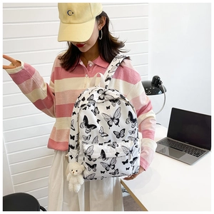 Detailed close-up of a white canvas backpack featuring a black butterfly pattern and plush bear charm