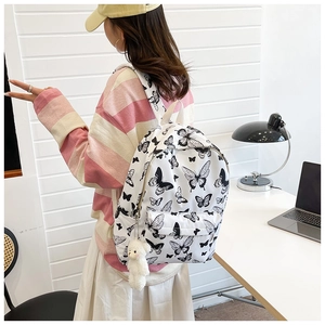 Detail of white butterfly print backpack for students featuring a plush bear charm on back