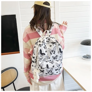 Close-up of white canvas backpack featuring black butterfly patterns and a plush bear charm