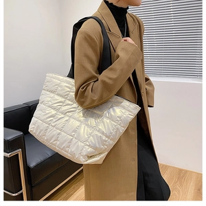 Quilted white puffer tote bag with wide black strap shown on a model in a modern room