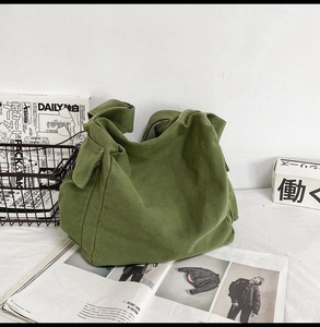 Close-up of grass green canvas messenger bag with flap pocket on a white display surface