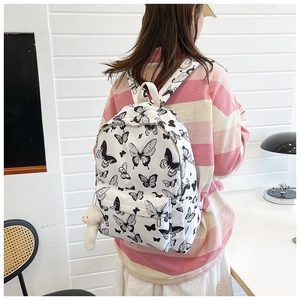 Detailed view of white butterfly pattern backpack featuring a cute teddy bear charm