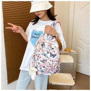 Close-up of white backpack with butterfly prints and a plush bear pendant on model