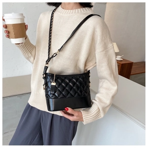 Detail of black quilted shoulder bag with chain strap and tassel on a model