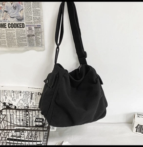 Detail of black canvas messenger bag featuring wide adjustable strap and side pocket