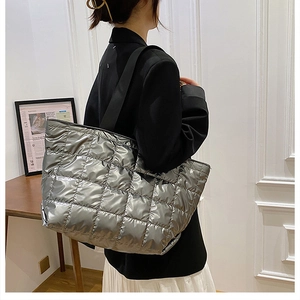 Silver metallic quilted puffer tote bag with wide black strap shown on shoulder