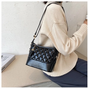 Detail view of black quilted crossbody bag with chain strap worn by a model
