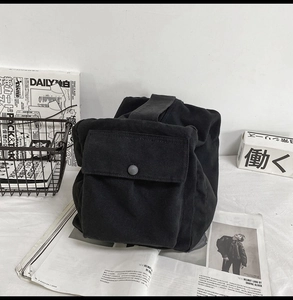 Detail of minimalist black canvas crossbody bag with a matte button flap on newspaper