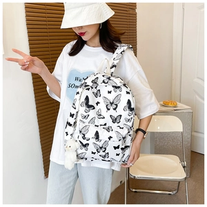 Close-up of white canvas backpack with black butterfly prints and cute plush bear pendant