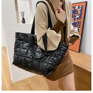 Detail of a black quilted puffer tote bag in glossy nylon fabric worn by a model