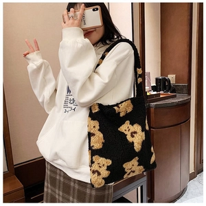 Detail of plush black tote bag with yellow teddy bear pattern worn by a model
