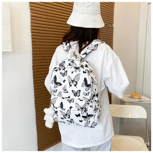 Close-up of white butterfly print backpack with plush ball accessory in a cozy room setting