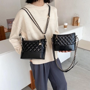 Chic black quilted hobo shoulder bag with a woven chain strap in a minimalist setting