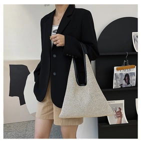 Detail of the woven cream tote bag featuring black leather shoulder straps on a model