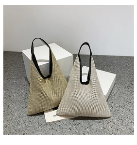 Detail of woven straw triangle tote bags in khaki and beige with black leather handles