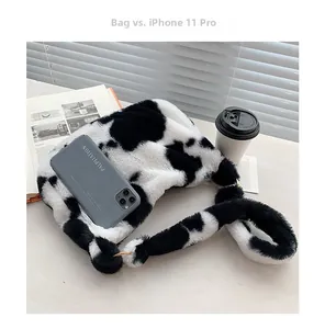 Plüsch-Schultertasche mit Kuhmuster Größenvergleich mit iPhone 11 Pro auf Tisch