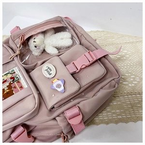 Detail of pink nylon backpack with multiple pockets, plush bear and good luck badge