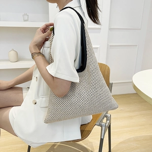 Minimalist woven straw shoulder bag with black strap worn by a woman in a studio