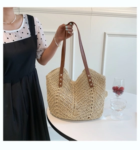 Detailed view of woven straw tote bag featuring brown leather straps and cross-stitch detail