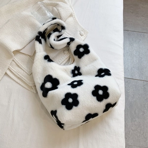 Close-up of soft white plush handbag with black flower pattern on minimalist fabric