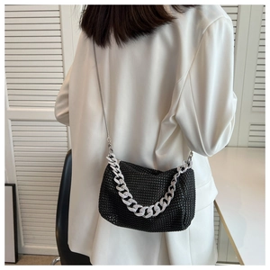 Close-up of a black rhinestone crossbody bag with silver chains on a white blazer