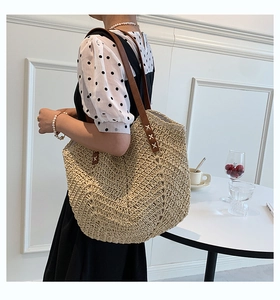 Detail of V-shape woven straw tote bag with brown leather straps and rivet stitching