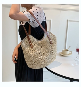Detail of hand-woven straw tote with brown leather shoulder strap and cross stitching