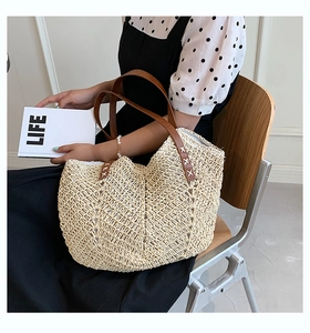 Close-up of beige straw woven tote bag with brown leather handles and stitching detail