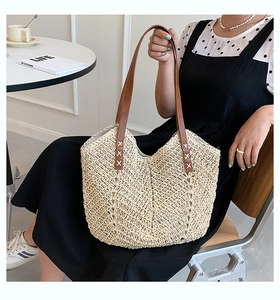 Detail of hand-woven straw tote bag showing brown leather straps with white stitching