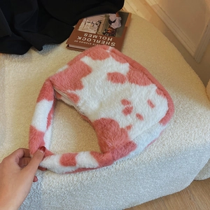 Detail showing the soft pink and white cow print plush texture and zipper of the shoulder bag