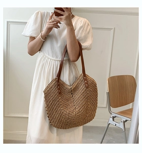 Macro detail of hand-woven straw tote with white cross-stitch and brown leather handle