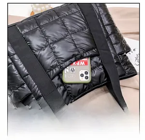 Detail showing the front slip pocket on a black quilted tote bag holding a smartphone