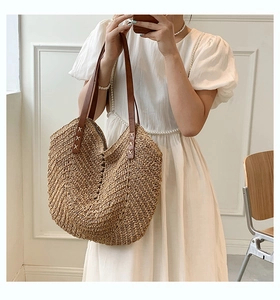 Close-up of woven straw tote bag featuring brown leather straps and detailed stitching