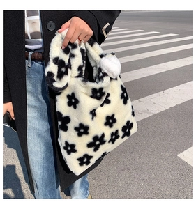 Detail of plush floral tote bag featuring black flower patterns and white fur ball pendant