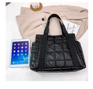Black quilted puffer tote bag with reinforced handles shown next to a tablet for size reference
