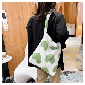 Detail of white plush tote bag with green heart pattern worn over shoulder in cozy interior