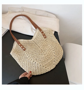 Close-up of handmade straw tote bag with brown leather straps and cross-stitch detail