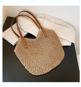 Detailed close-up of handmade straw tote bag with brown leather handles and white stitching