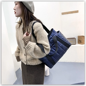 Close-up of navy blue quilted tote bag with black strap and soft glossy texture