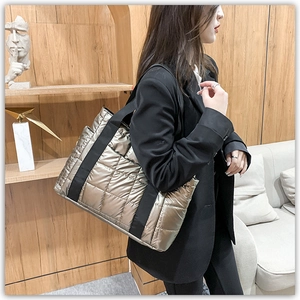 Detail of quilted metallic bronze tote bag with black canvas strap shown on a model