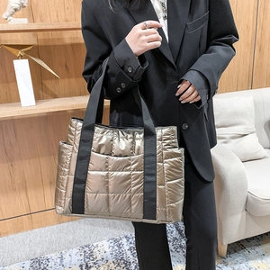 Detail of champagne gold quilted tote bag showing silky metallic texture and black straps