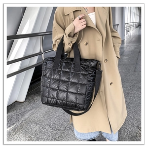 Close-up detail of quilted black down tote bag with nylon texture and reinforced handles